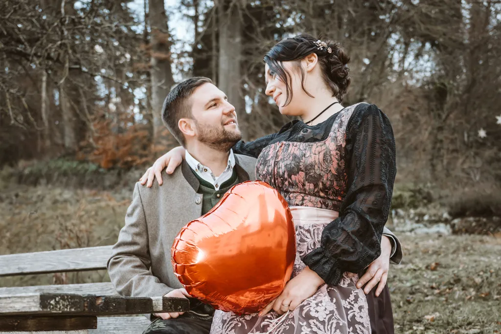 Verliebtes Brautpaar: Sie auf seinem Schoß mit Luftballon. Braut sitzt auf dem Schoß des Bräutigams, hält Luftballon, Arm um seine Schulter.