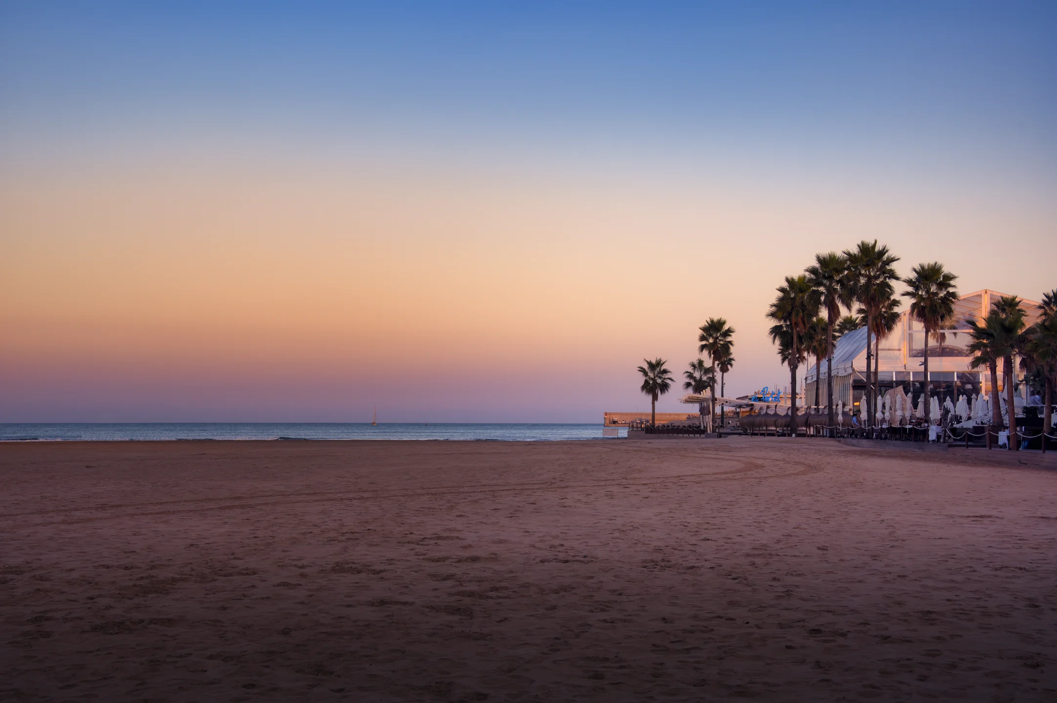 Sonnenuntergang am Strand. Auf der rechten Seite eine Strandbar mit Palmen.