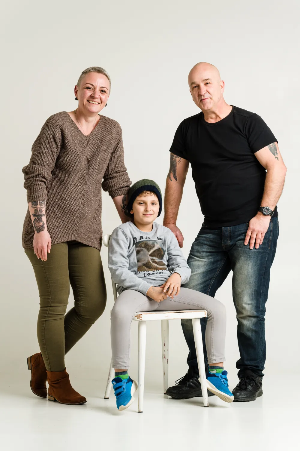 Norbert Kreidt mit seiner Familie Ein Familienporträt. Die Mutter und der Vater stehen, während ihr Sohn, ein kleiner Junge, auf einem weißen Stuhl sitzt.